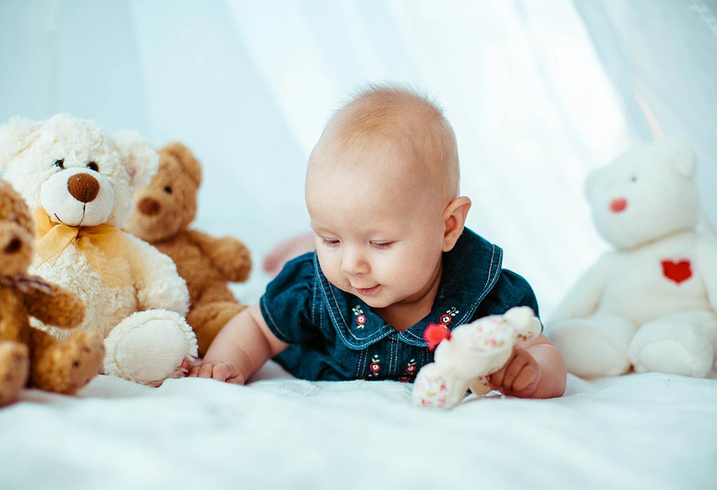 A baby girl playing with soft toys in bed